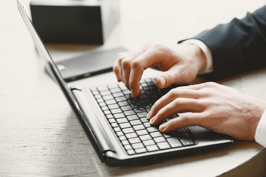 Business professional typing on a laptop at a desk with a smartphone nearby.